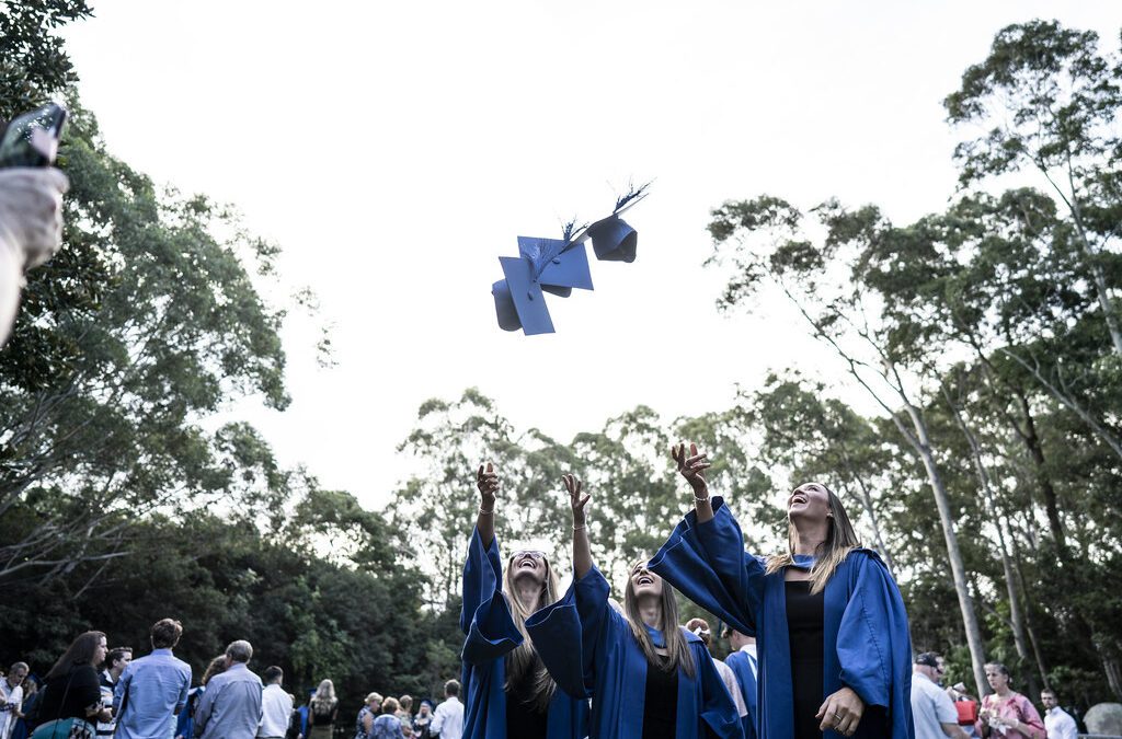 Three female UOW students celebrate graduating by throwing their hats in the air.
